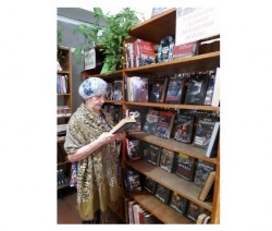 На фото изображена женщина с книгой возле стеллажа с выставкой книг