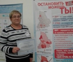 На фотографии изображена заведующая городской библиотекой-сектором №17 Аношина М.В., на фоне плаката про ВИЧ с сертификатом о пройденном обучении в руке